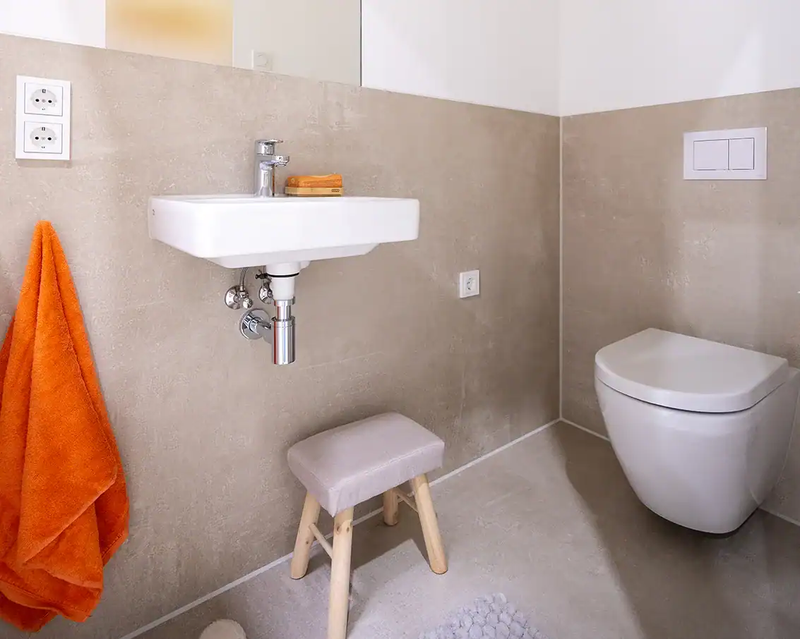 Sauberes Badezimmer mit moderner Toilette und Wandwaschbecken, inklusive Handtuchhalter und Steckdosen.
